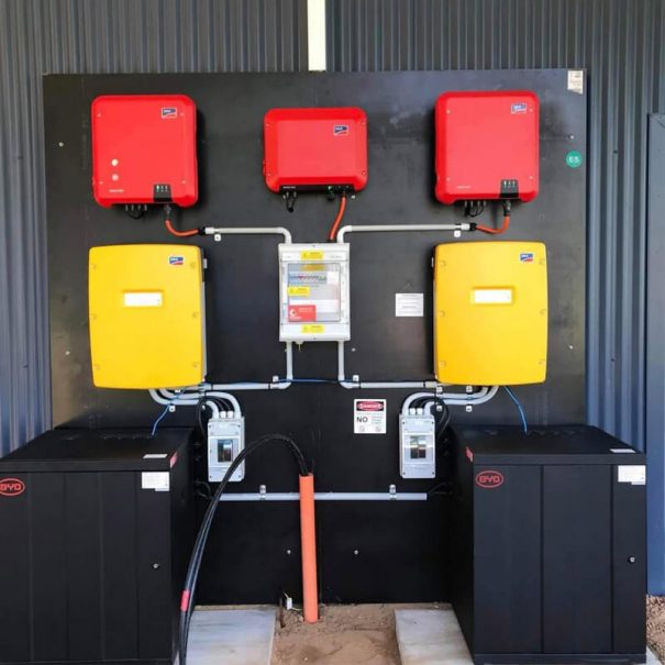 An image showing part of the solar power system set up at Tree Chalets. There are 3 red inverters, 2 yellow inverters and 2 black battery boxes.