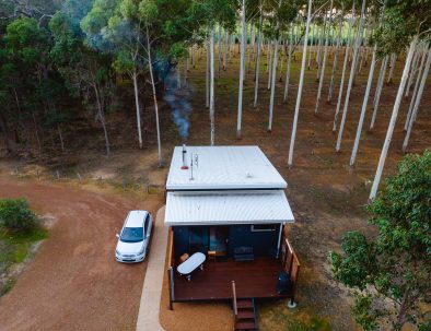 Image 3: An overhead view of Chalet Rosegum. There is an outdoor bath on the back deck and a car parked at the chalet. There is smoke coming from the chimney in the chalet.
