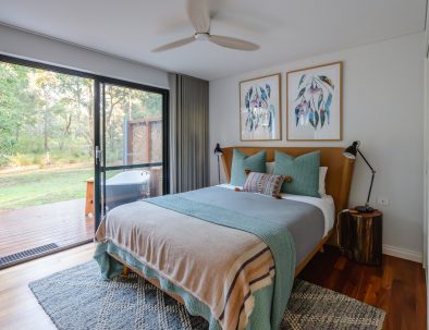 Image 5: The bedroom in the chalet. The bed has large pillows, bedside lamps and there is a ceiling fan. The outdoor bath is just outside and can be accessed from the bedroom glass sliding door.