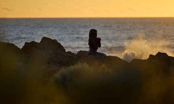 A statue depicting a young Indigenous woman sitting on the rocks looking out to sea and waiting for someone.