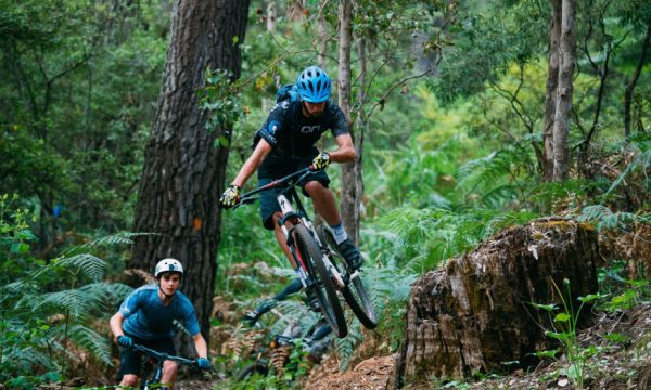 2 young men riding mountain bikes through the forest